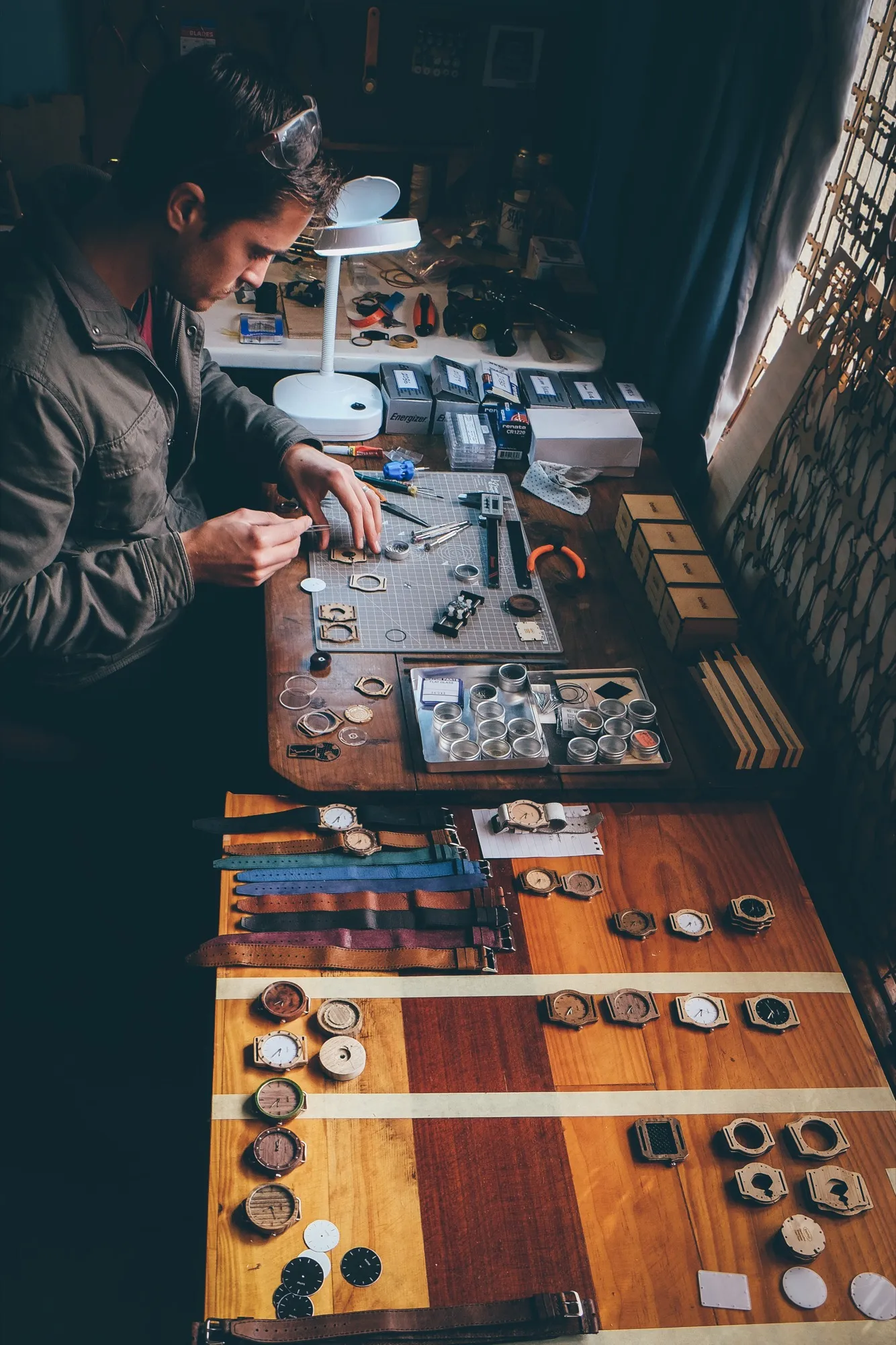 Rows of finished watch cases in different wood tones, with dials and straps laid out on the workbench